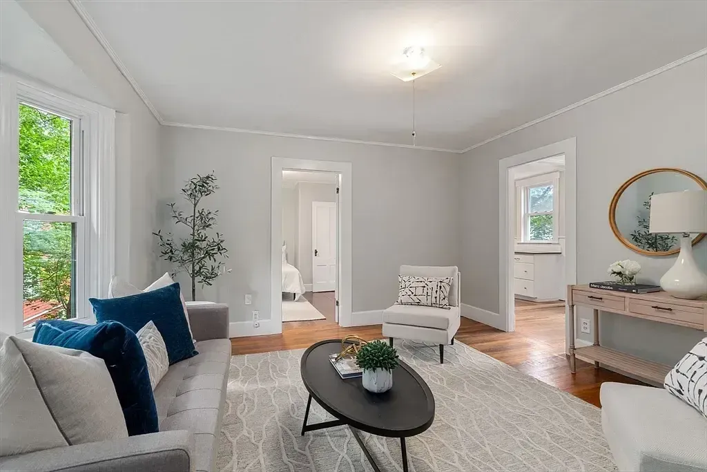 A bright living room featuring a grey sofa, hardwood floors, an area rug, and multiple doorways leading to other rooms.