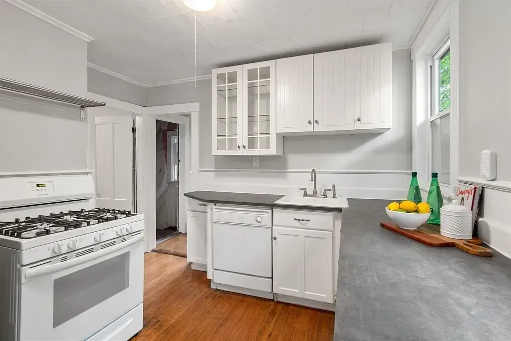 A kitchen featuring white cabinetry, a gas range, dishwasher, sink, and hardwood floors.